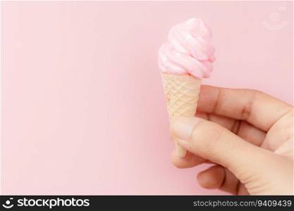 Woman&rsquo;s hand holding meringue ice cream cone on pink background for sweet and refreshing dessert concept