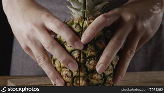 Woman&rsquo;s hand show two halves of fresh ripe natural organic juicy tropical fruit pinapple on acutting board on a wooden background. Motion, 4K UHD video, 3840, 2160p. Concept of vegetarian diet eating.. Fresh juicy ripe halves of natural organic pineapple in a woman&rsquo;s hands on a cutting board on a wooden table. Motion, 4K UHD video, 3840, 2160p.