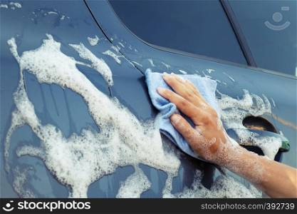 Woman's hand with a blue sponge in a soapy foam washes the car