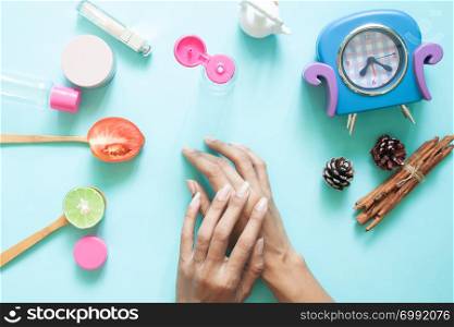 Woman&rsquo;s hands applying lotion on skin. Cosmetic containers and natural ingredient on pastel background