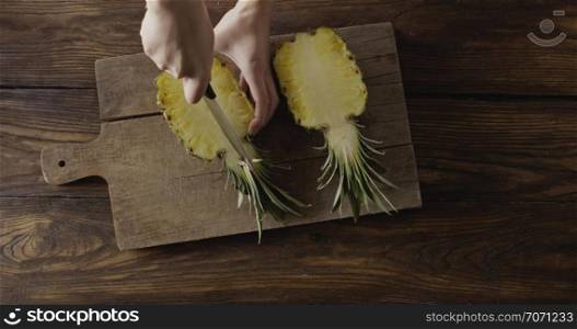 Woman&rsquo;s hands are cutiing the halves of fresh yellow natural tropical pineapple in a quater. Four parts of fruit on a cutting board on a wooden table. Top view. Motion, 4K UHD video, 3840, 2160p.. Female&rsquo;s hands cut the halves of fresh juicy yellow natural exotic pineapple in a quater on a wooden cutting board. Top view. Motion, 4K UHD video, 3840, 2160p.