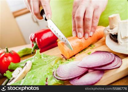 Woman&rsquo;s hands cutting carrot, behind fresh vegetables.
