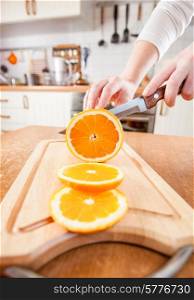 Woman&rsquo;s hands cutting fresh orange on kitchen