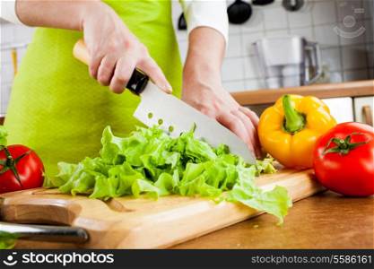 Woman&rsquo;s hands cutting lettuce, behind fresh vegetables.