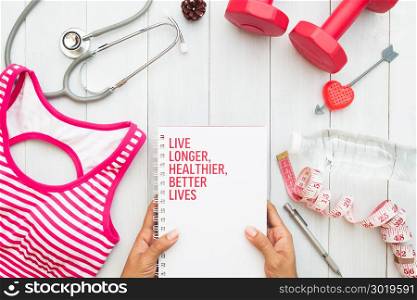 Woman&rsquo;s hands holding book, fitness equipments and stethoscope on white wooden background, top view, Healthy lifestyle concept