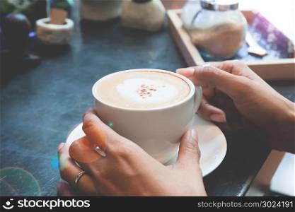 Woman&rsquo;s hands holding cup of hot cappuccino in cafe