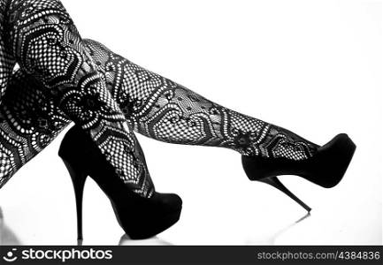 Woman&rsquo;s legs with pattern nylons and high heels photographed over a reflective surface and a white background.