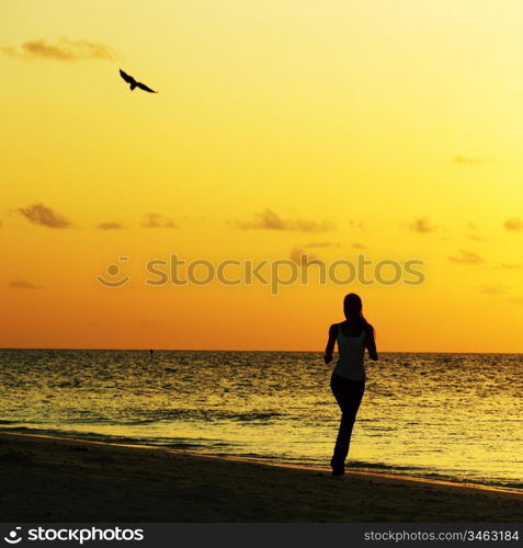 woman run along the sea coast of sunrise behind