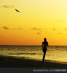 woman run along the sea coast of sunrise behind