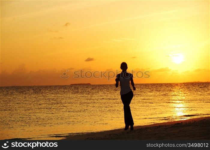 woman run along the sea coast of sunrise behind