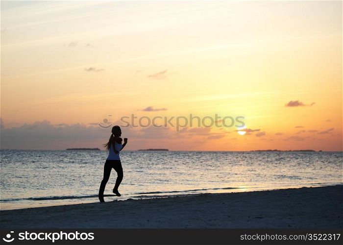 woman run along the sea coast of sunrise behind