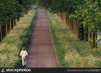 Woman running down remote country lane bordered by wildflowers and trees
