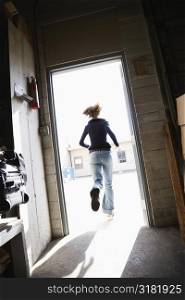 Woman running through open door from building to sunny outside.