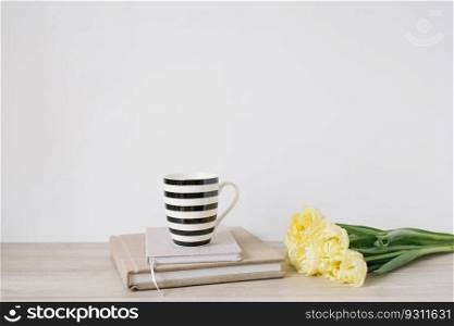 Woman’s coffee break at workplace. A mug, a bouquet of tulips and notepads for notes on the table. Copy space