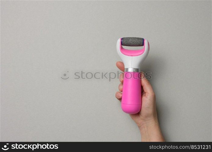 Woman’s hand holding an electric pedicure tool on a gray background
