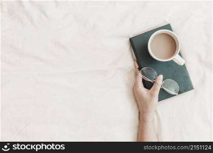 woman s hand holding book with eyeglasses hot drink it