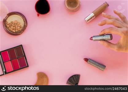 woman s hand holding lipstick various make up accessories pink background