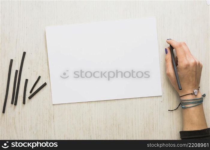 woman s hand holding natural charcoal stick with blank white paper wooden background