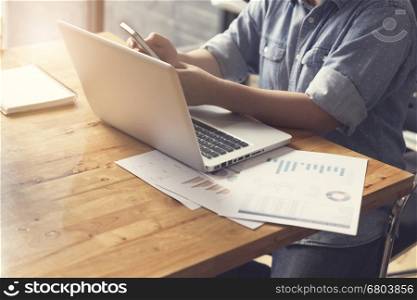 woman's hand holding smartphone with laptop computer and business document, selective focus and vintage tone