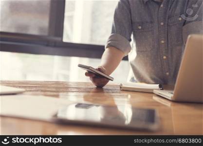 woman's hand holding smartphone with laptop computer for working concept, selective focus and vintage tone