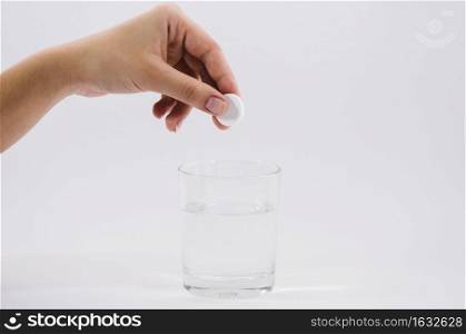 woman s hand holding white pill glass water against grey backdrop