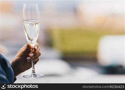 Woman s hand holds glass of white wine, celebrates something together with friends, blurred background with copy space for your promotional text or advertisement.