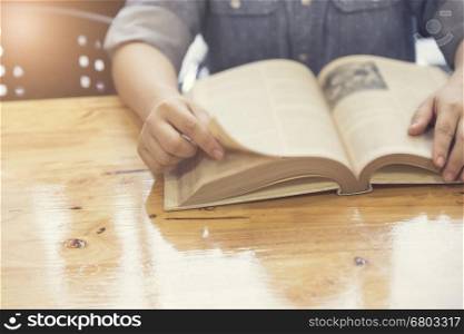 woman's hand reading book on wooden table, selective focus and vintage tone
