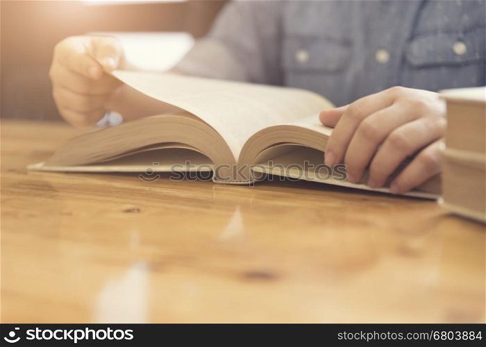 woman's hand reading book on wooden table, selective focus and vintage tone