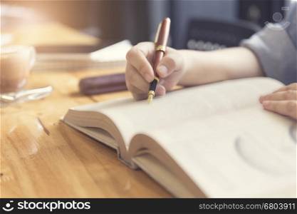 woman's hand reading book with pen, tablet and notebook on wooden table, selective focus and vintage tone