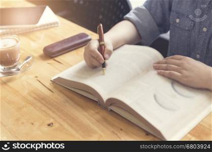 woman's hand reading book with pen, tablet and notebook on wooden table, selective focus and vintage tone