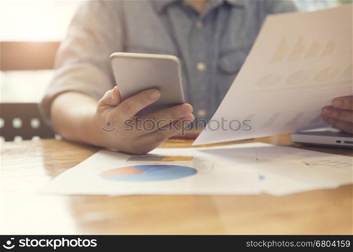woman's hand working with mobile phone, business document and laptop computer notebook for working concept, selective focus and vintage tone