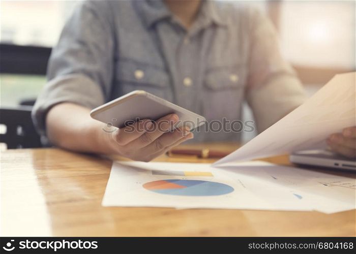 woman's hand working with mobile phone, business document and laptop computer notebook for working concept, selective focus and vintage tone