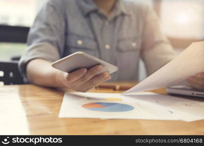 woman's hand working with mobile phone, business document and laptop computer notebook for working concept, selective focus and vintage tone