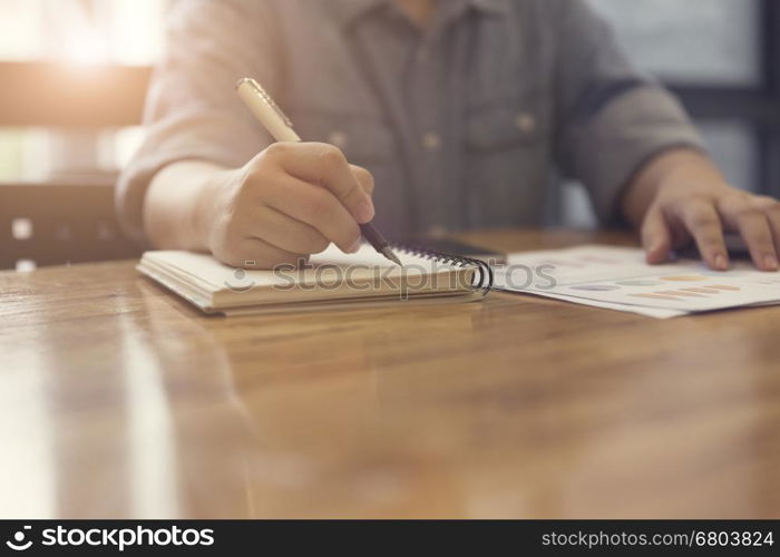 woman's hand writing on notebook with business document for working concept, selective focus and vintage tone