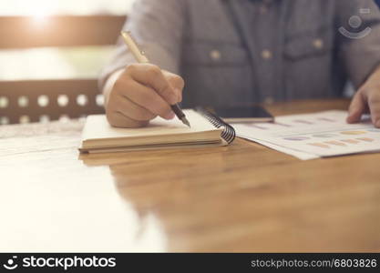 woman's hand writing on notebook with business document for working concept, selective focus and vintage tone