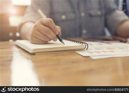 woman's hand writing on notebook with business document for working concept, selective focus and vintage tone