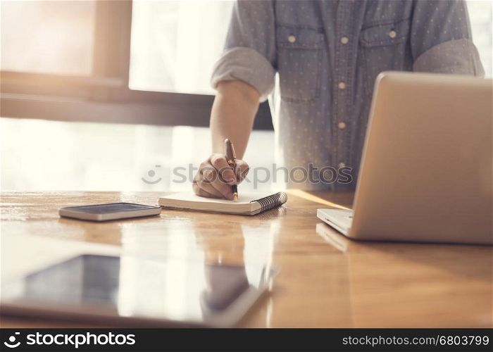 woman's hand writing on notebook with laptop computer for working concept, selective focus and vintage tone