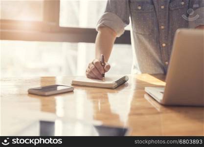 woman's hand writing on notebook with laptop computer for working concept, selective focus and vintage tone