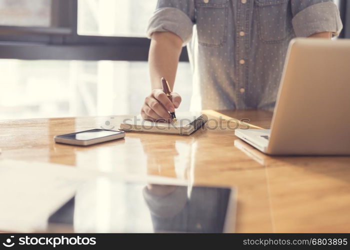 woman's hand writing on notebook with laptop computer for working concept, selective focus and vintage tone