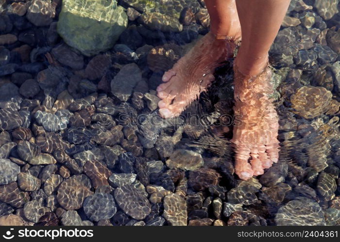 Woman?s legs ankle-deep in clear water. Ripple patterns reflect light on water over pebbles