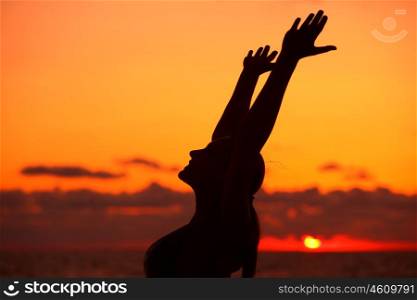 Woman's silhouette on sunset background, doing yoga exercise outdoors on the beach in the evening, enjoying life, happy summer holidays