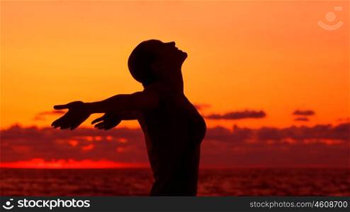 Woman's silhouette on sunset background, happy girl with raised hands standing on the beach and looking up in the sky, enjoying summer vacation&#xA;