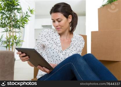 woman sat amongst cardboard boxes looking at digital tablet