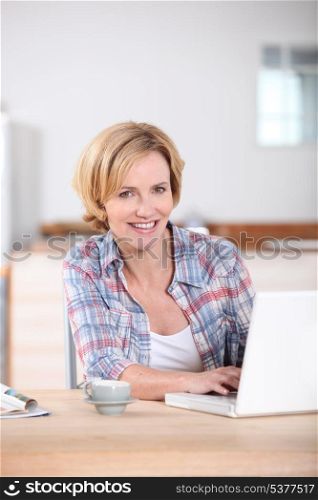 Woman sat in kitchen typing on laptop computer