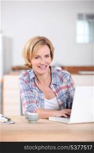Woman sat in kitchen typing on laptop computer