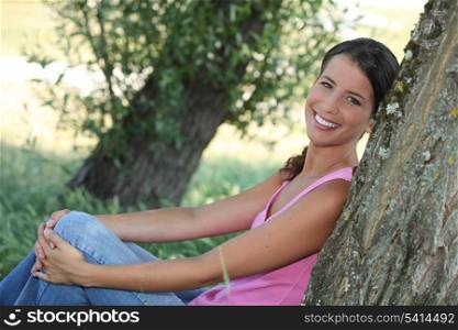 Woman sat leaning against tree trunk