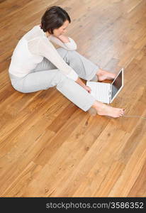 Woman sat on wood panel floor using laptop