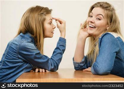 Woman saying bad things about her over confient female friend. Pointing at forehead, stupidity gesture.. Woman mocking her confident friend