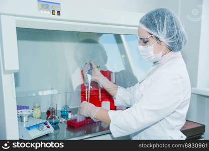 Woman scientist in a white protective clothing conducts research in a lab