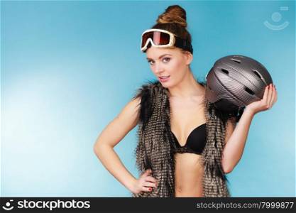 Woman seductive girl in ski googles holds helmet. Woman sexy hot skier girl wearing black bra fur vest ski googles holding helmet. Winter sport activity. Beautiful seductive sportswoman on blue studio shot